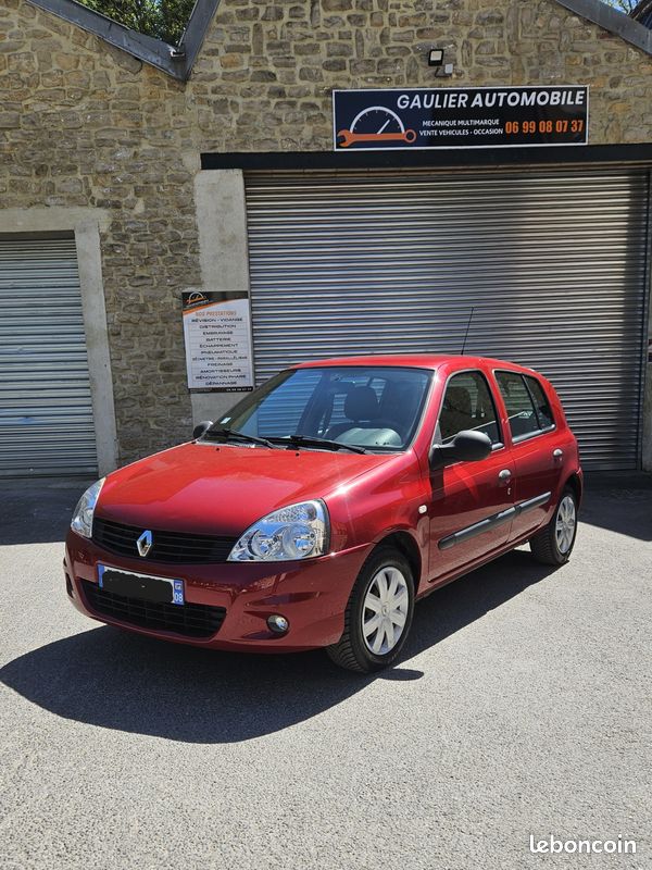 Red Renault hatchback parked in front of a stone auto shop with a closed metal shutter and sign above the door (Gaulier Automobile).