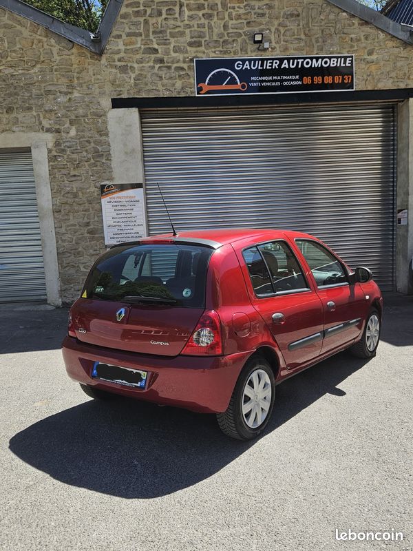 426568ba8c5ccafad1111330886ae562b9ca57d1 - Gaulier Automobile Red Renault hatchback parked in front of a stone building with a closed metal shutter and a sign reading 'GAULIER AUTOMOBILE' above the door.